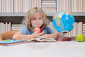 School boy with books and apple in library. Cute pupil looking at globe in library at the elementary school. School