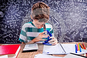 School boy at the desk with microscope, big blackboard