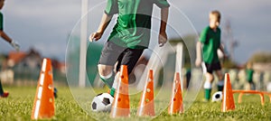 School boy dribbling soccer ball in slalom training drill. Football training camp for school kids