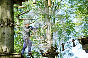 School boy in forest adventure park. Acitve child, kid in helmet climbs on high rope trail. Agility skills and climbing