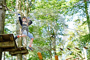 School boy in forest adventure park. Acitve child, kid in helmet climbs on high rope trail. Agility skills and climbing