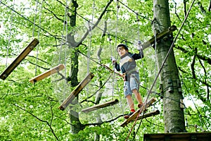 School boy in forest adventure park. Acitve child, kid in helmet climbs on high rope trail. Agility skills and climbing