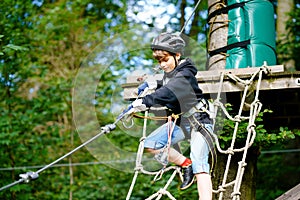 School boy in forest adventure park. Acitve child, kid in helmet climbs on high rope trail. Agility skills and climbing