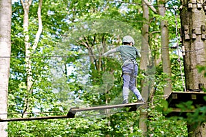 School boy in forest adventure park. Acitve child, kid in helmet climbs on high rope trail. Agility skills and climbing