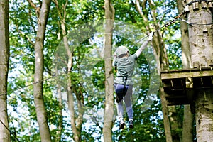 School boy in forest adventure park. Acitve child, kid in helmet climbs on high rope trail. Agility skills and climbing