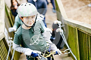 School boy in forest adventure park. Acitve child, kid in helmet climbs on high rope trail. Agility skills and climbing