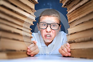 School boy in glasses sitting between two piles of books and loo