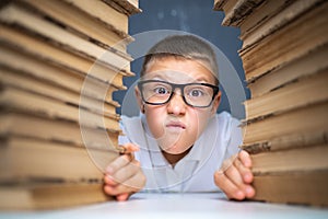 School boy in glasses sitting between two piles of books and loo