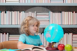School boy looking at globe in library, geography lesson. School child student learning in class, study english language