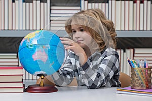 School boy looking at globe in library, geography lesson. School child student learning in class, study english language