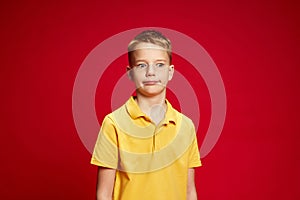 School-boy looks away disdainfully, dressed vibrant yellow T-shirt against red studio background.