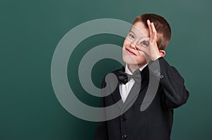 School boy show ok sign, portrait near green blank chalkboard background, dressed in classic black suit, one pupil, education conc