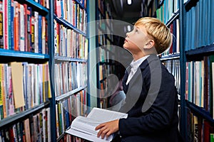 school boy sits in library looking up at books shelves