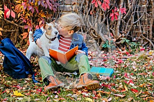 School boy sitting on bright colorful leaves kissing and hugging his dog in the fall autumn park, outdoor. Happy child with puppy