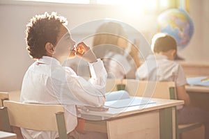 School boy sitting in desk and thinking while writing exam