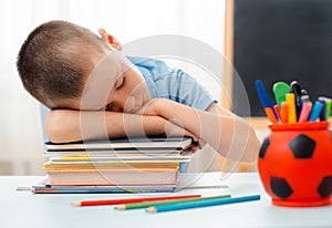 School boy sitting at home classroom lying desk filled with books training material schoolchild sleeping lazy bored