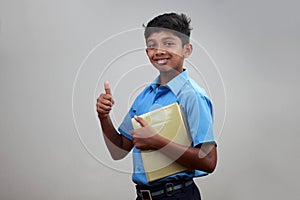 A school boy wearing uniform holds note books in hand