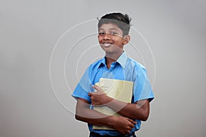 A school boy wearing uniform holds note books in hand