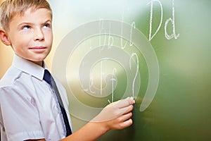 School boy writes English alphabet with chalk on blackboard