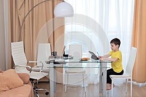 School boy in yellow t-shirt sitting at the table with digital tablet studying at home. Distance learning online