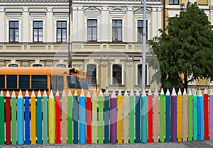 School bus, colorful pencils fence, Victorian building.