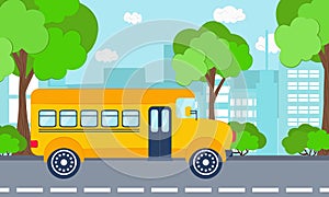 School bus rides along the road, buildings and trees in the background.