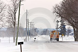 School Bus Travelling Down a Country Road with Snowdrifts and Blowing Snow in Winter