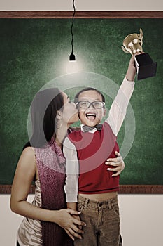 School champion holding trophy kiss by mum in class