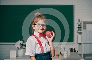 School child hold apple with funny expression against blackboard. Kids education and knowledge.