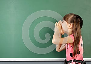 School child shouting near blank school blackboard, copy space