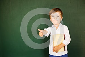 School child thumbs up and hold book over blackboard. Free text, copy space