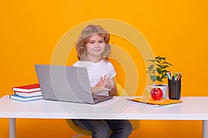 School child using laptop computer. Portrait of cute child school boy, isolated on yellow studio background. School and