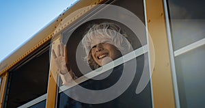 School child waving out school bus window closeup. Boy saying goodbye to mother.