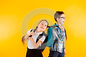 School children, boy and girl with backpacks isolated on yellow