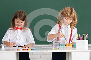 School children drawing a colorful pictures with pencil crayons in classroom on blackboard background. Portrait of cute