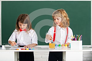 School children drawing a colorful pictures with pencil crayons in classroom. Cute pupils enjoying art and craft lesson.