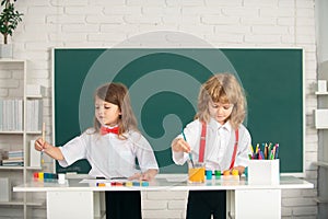 School children girl and boy painting with paints color and brush in classroom. Cute kids draw with colorful crayons.