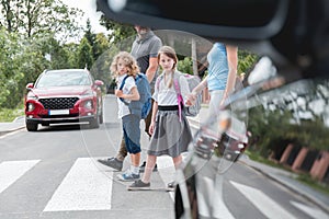 School children goes through the pedestrian crossing in the street, right in front of the car