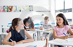 School children sitting at the desk in classroom on the lesson, talking.