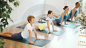 School children and their parents exercising on mats in Cobra position during family yoga training in gym fitness center