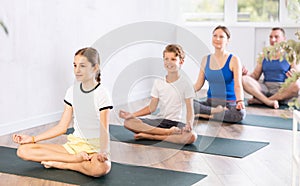 School children and their parents sitting on mats in Lotus pose during family yoga training in gym fitness center