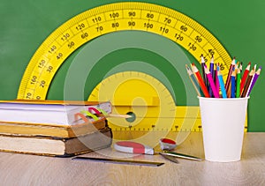 School concept: colore pencil, book, ruler, scissors and green chalkboard with yellow protractor. photo