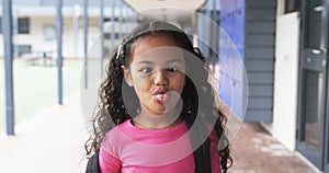 In a school corridor, a young African American girl sticks out her tongue