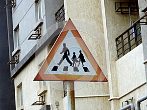 A school crossing sign at the side of the road to inform drivers to be alert of children crossing the street, school children