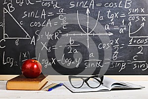 School desk in classroom, with books on background of chalk board with written formulas. Soncept Teacher`s Day