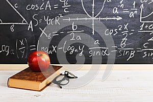 School desk in classroom, with books on background of chalk board with written formulas. Soncept Teacher`s Day