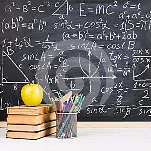 School desk in classroom, with books on background of chalk board with written formulas. Soncept Teacher`s Day