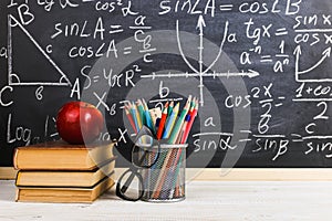 School desk in classroom, with books on background of chalk board with written formulas. Soncept Teacher`s Day