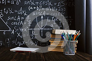 School desk in classroom, with books on background of chalk board with written formulas. Soncept Teacher`s Day