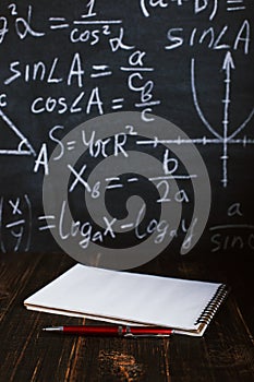 School desk in classroom, with books on background of chalk board with written formulas. Soncept Teacher`s Day